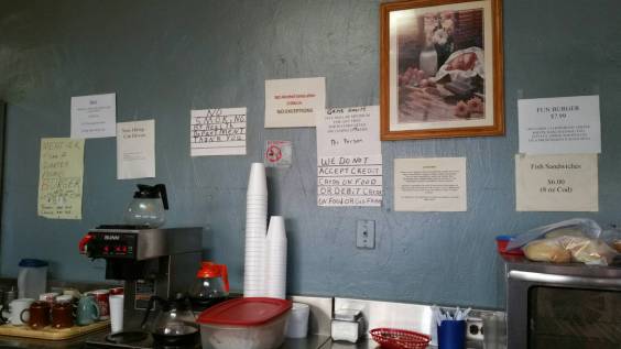 A restaurant counter and wall with many hand written signs.